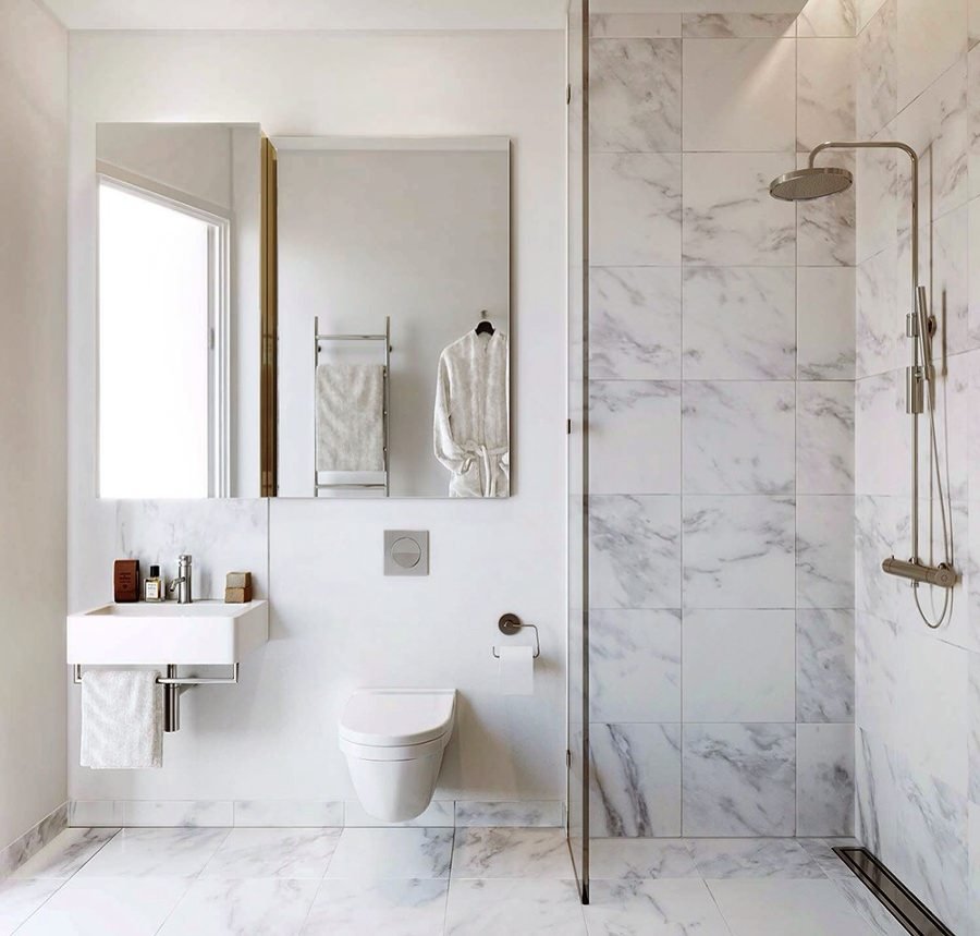 Piccolo ma elegante bagno che utilizza il marmo bianco su pavimento e zone d’acqua. Interessante idea per il taglio di luce che illumina la doccia