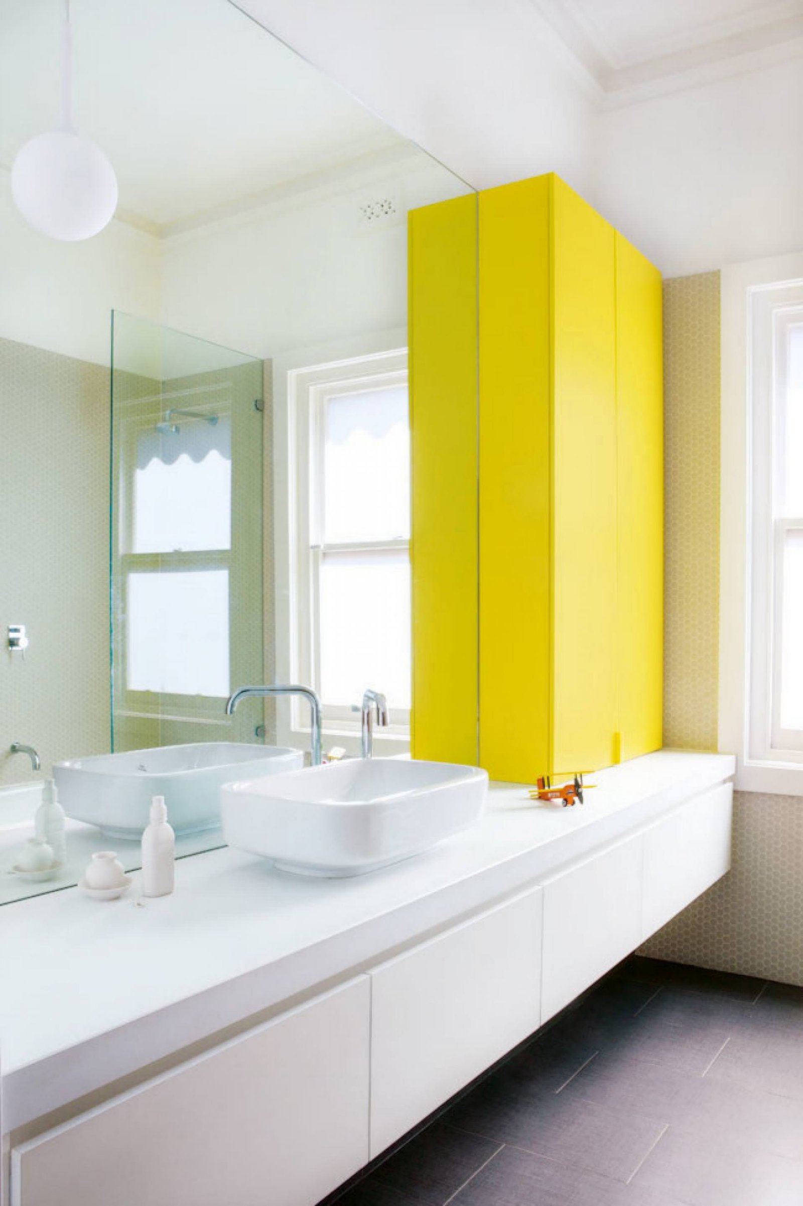 Le finiture bianche aiutano a tenere il bagno luminoso e pulito, ma l'armadio di colore giallo lo rende allegro e moderno