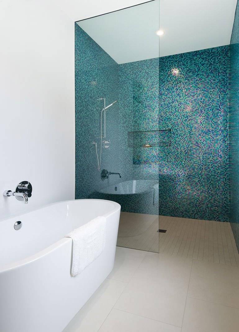 Stupendo mosaico blu scuro con riflessi dorati in questo moderno bagno minimal con vasca in ceramica bianca e box doccia