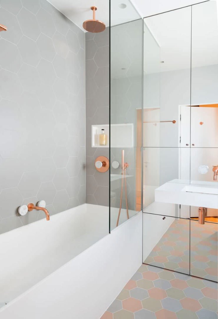 Immagine piccolo bagno moderno, stile scandinavo, con doccia e vasca. Colori tenui in una combinazione di grigio e rame. Perfetta l'idea dello specchio a tutta parete che ingrandisce lo spazio. Idee progettazione bagni piccoli, costi ristrutturazione e arredo.
