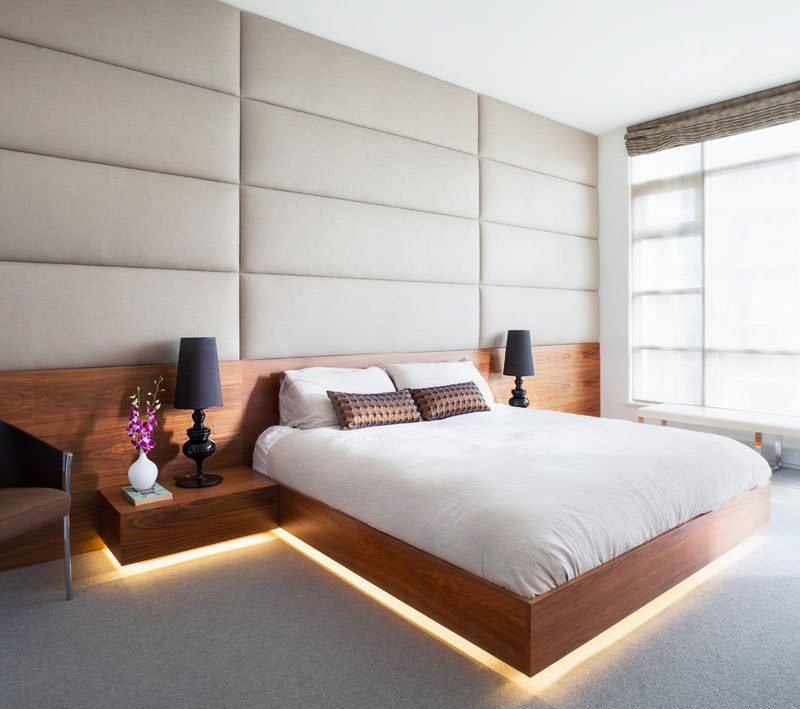 Camera da letto moderna con stupendo effetto scenico con un sistema di illuminazione sotto il letto. Parete testata rivestita in tessuto, pavimento in legno sbiancato.