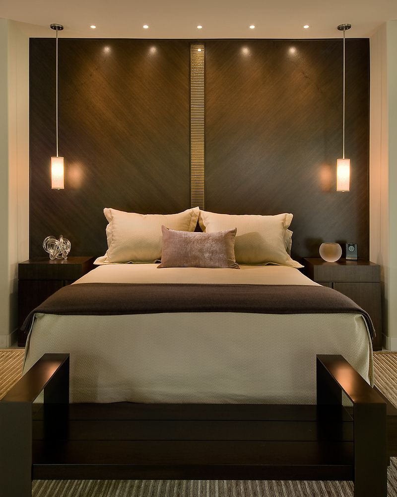 Camera da letto contemporanea con la testiera creata dal rivestimento in legno marrone scuro della parete. Luci moderne ed eleganti