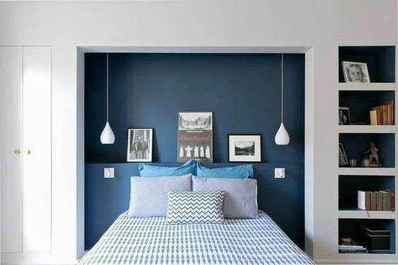 Camera da letto moderna con la testiera incassata in parete in cui gli elementi d’arredo acquistano il risalto degli oggetti incorniciati. Spiccano l’eleganza del blu di Prussia e la simmetria delle lampade sospese.