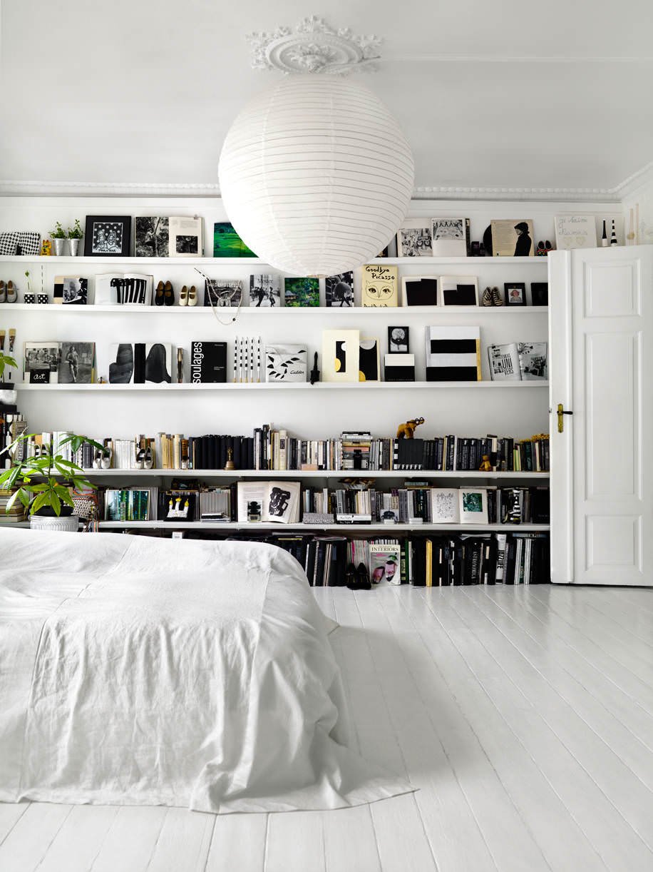 Bellissima camera da letto total white in cui i libri della libreria su una parete aggiungono colore alla stanza - pavimento in legno verniciato in bianco