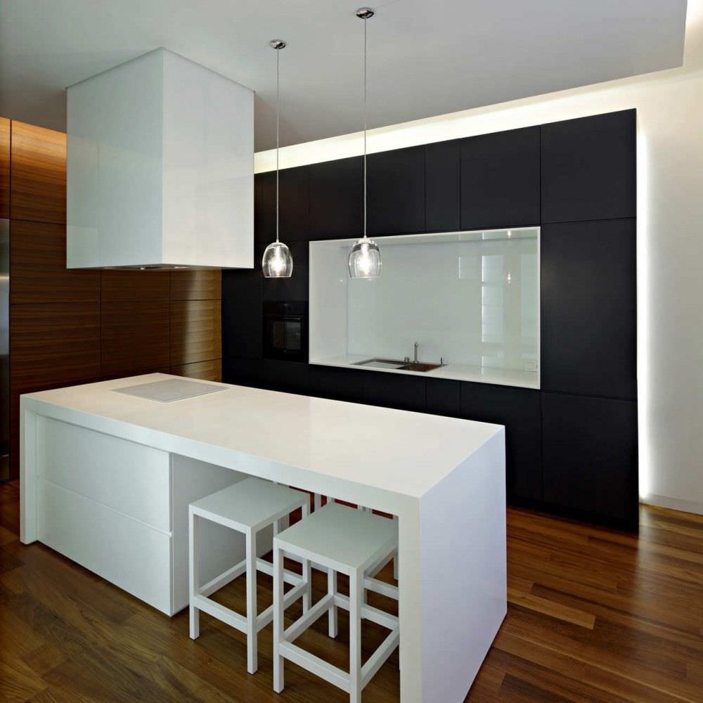 Idee progettazione cucine moderne in bianco e nero con isola che fa anche da tavolo. Soluzione con due sedie per parte e piano cottura ad induzione. Illuminazione perimetrale sul soffitto e inserita sui lati della parete attrezzata.