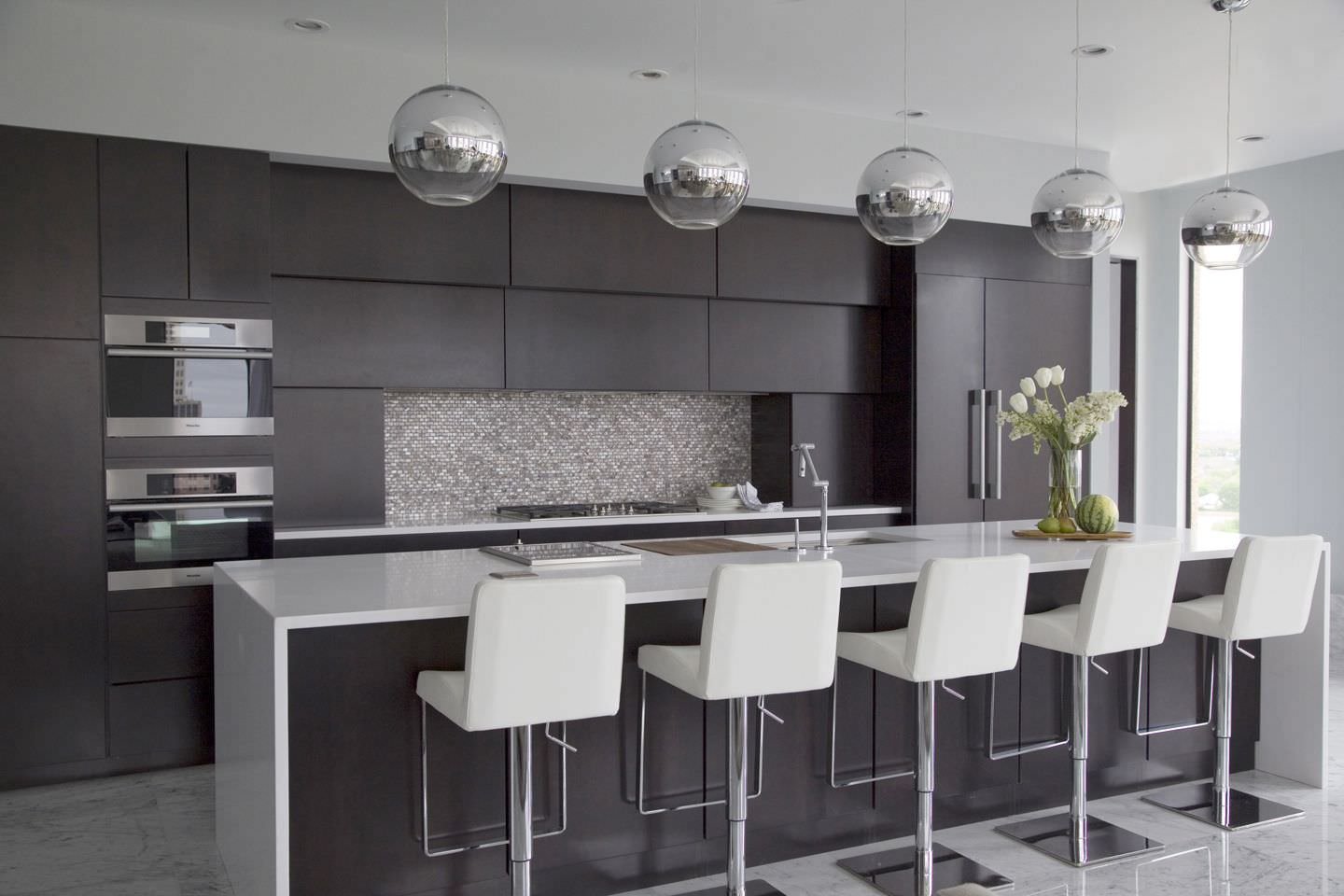 Cucina con isola elegante e lineare con il nero colore dominante. Il top e le sedute dei sgabelli in grigio chiaro, così come anche il pavimento in marmo.