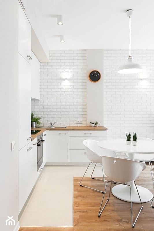 Immagine cucina moderna bianca con mobili in laminato, top in legno, parete in mattoni bianchi e pedana in resina.