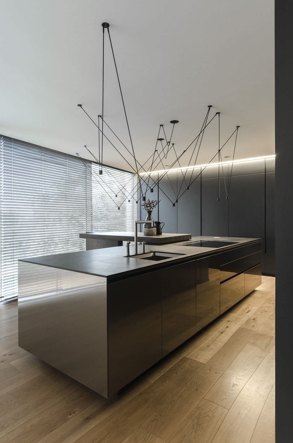 Bellissima cucina moderna in acciaio inox con top in quarzo di colore nero. Particolare illuminazione con lampade a sospensione e pavimenti in legno.
