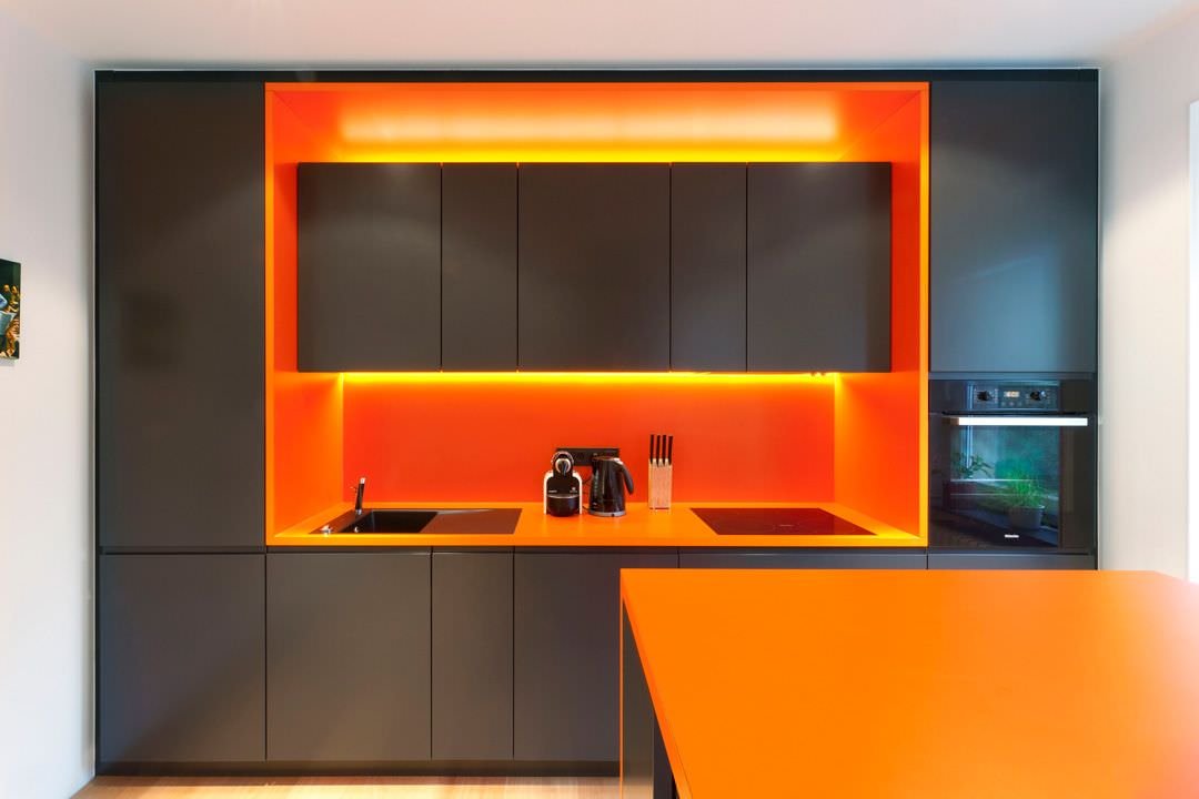 Piccola cucina moderna nei colori nero e arancione. Parete attrezzata in laminato con luci a led intorno alla dispensa per un look futuristico.