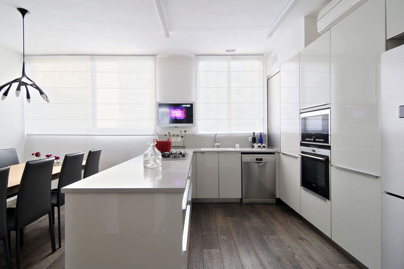Luminosa cucina moderna ad U con mobili in laminato laccato bianco, top in quarzo e pavimenti in legno scuro.