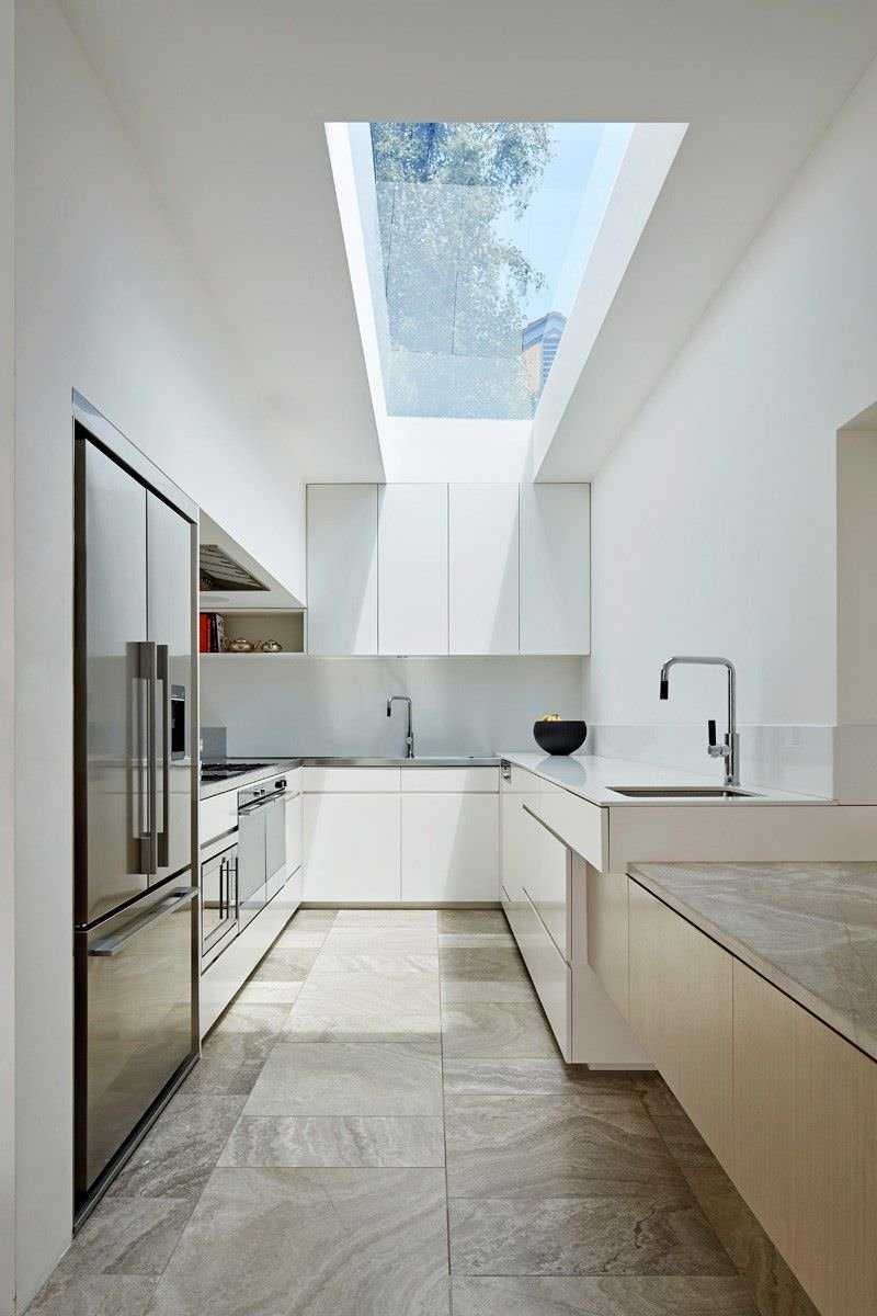 Luminosa cucina moderna con grande vetrata sul soffitto, spazio ideale per cucinare in un ambiente funzionale ed elegante. Mobili bianchi e pavimenti in travertino