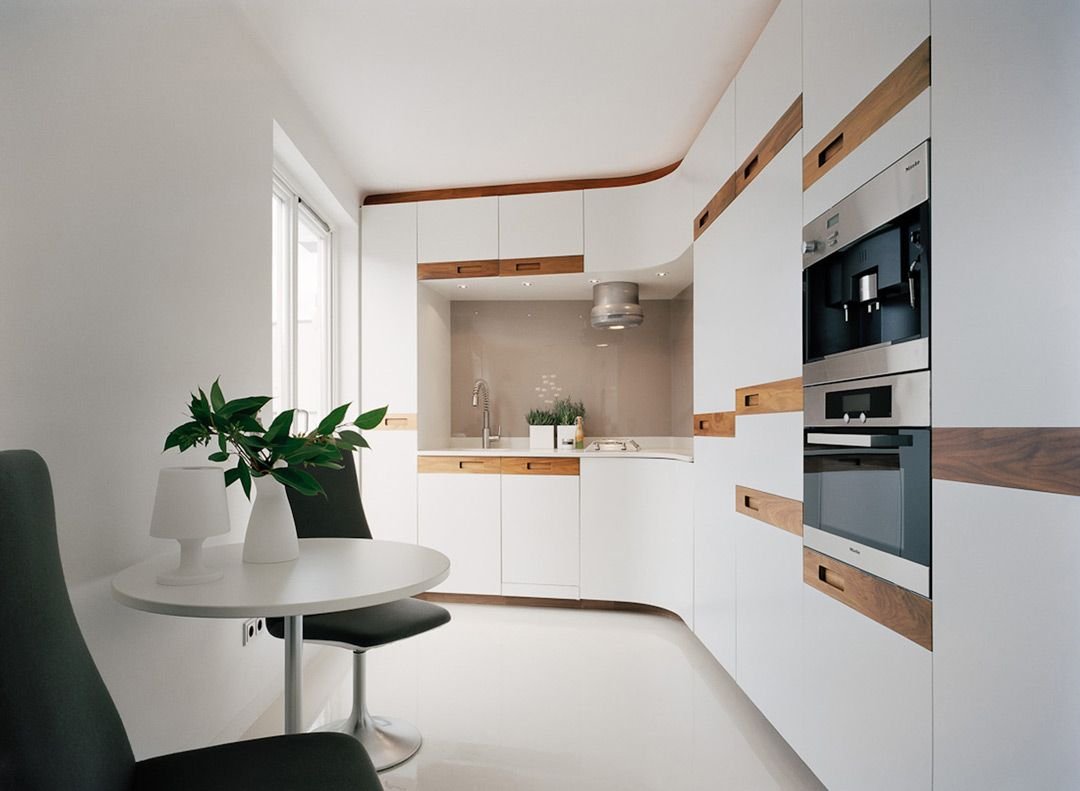 Stupendo layout per questa piccola cucina moderna con il profilo curvo che ammorbidisce lo spazio. Realizzata in laminato bianco con inserti in legno. Pavimento bianco in resina.