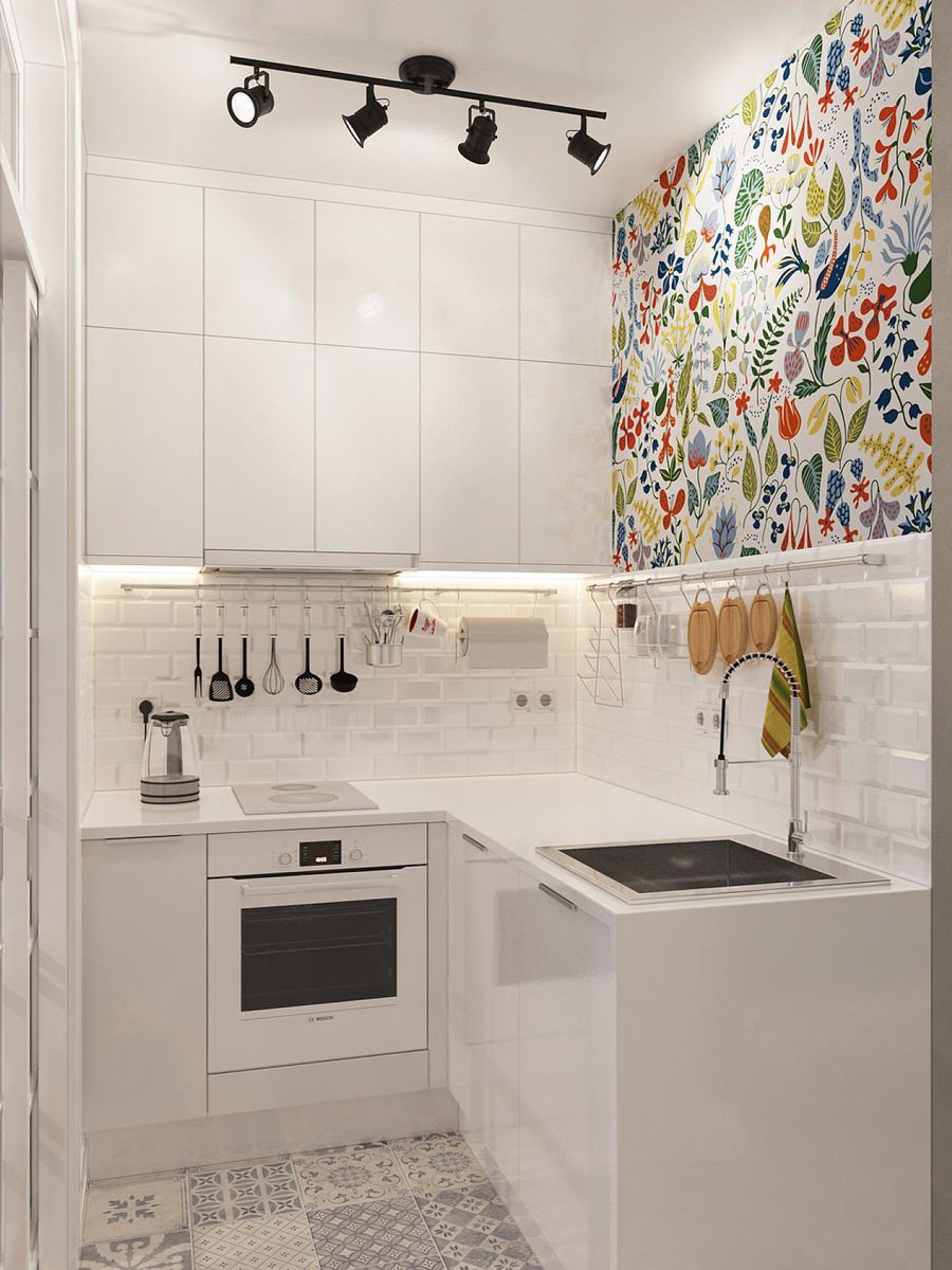 Piccola cucina bianca in cui la parete decorata fa una bella differenza. Una coloratissima carta da parati offre allegria e vitalità allo spazio. Un tocco semplice, moderno e originale. Pavimento in piastrelle patchwork.