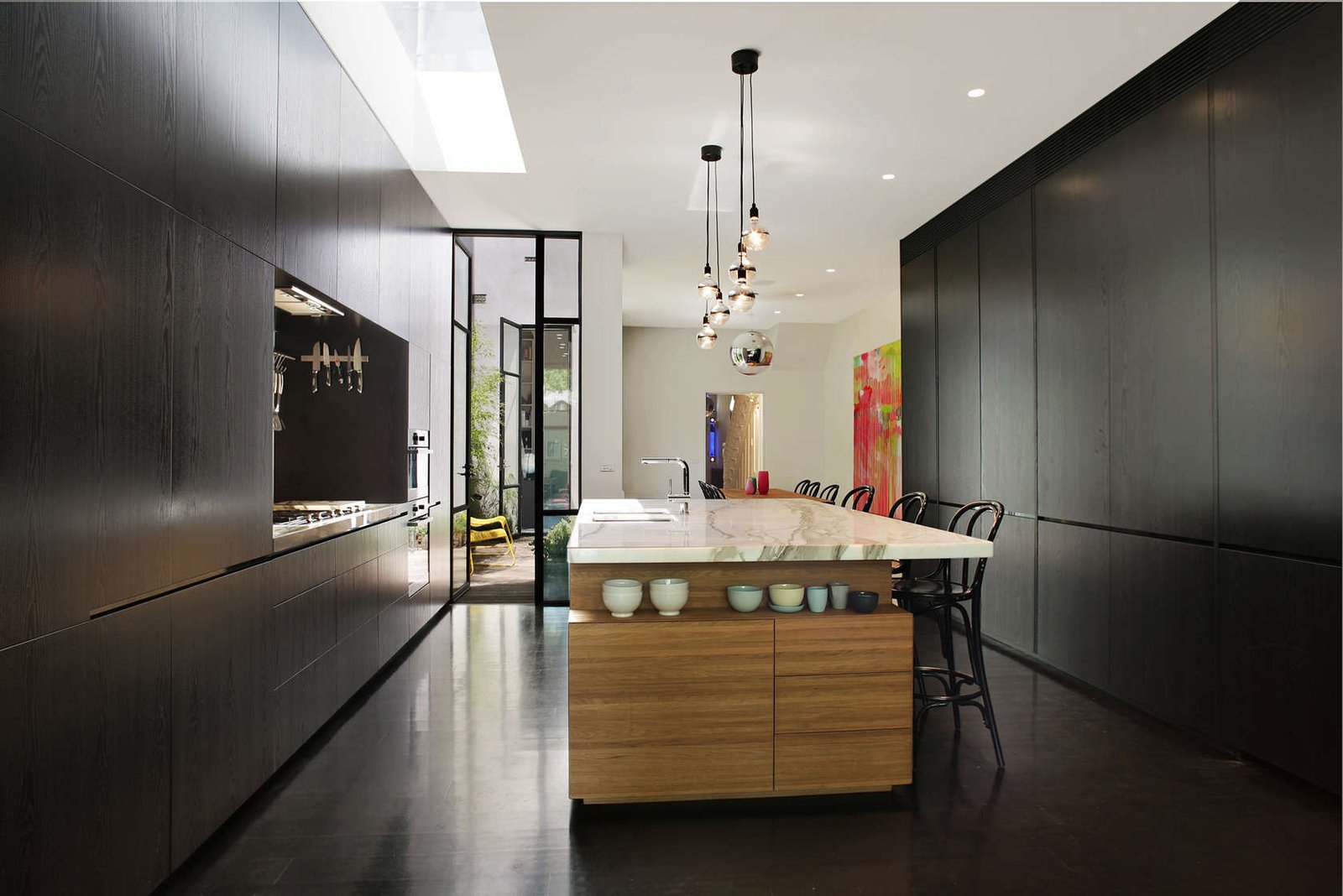 Ambiente moderno con mobili massicci di colore nero, pavimenti in cemento effetto lucido, isola in noce con piano in marmo - design cucine moderne