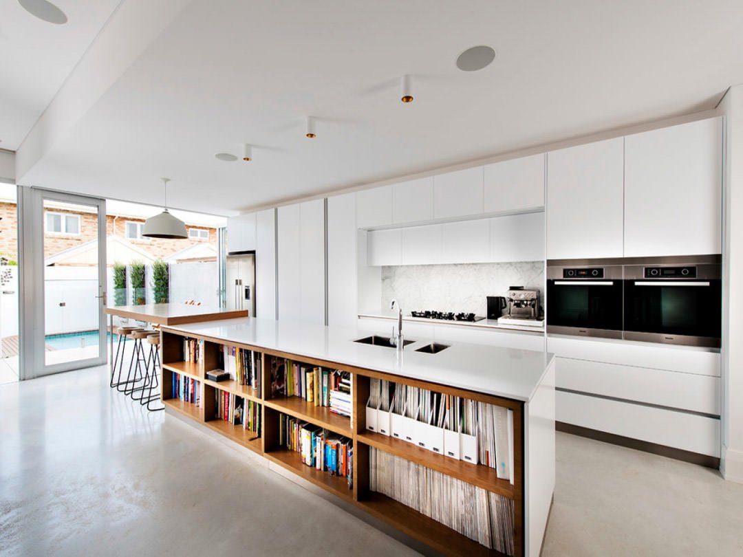 Cucina moderna aperta sul soggiorno con mobili bianchi e isola rivolta verso l’esterno