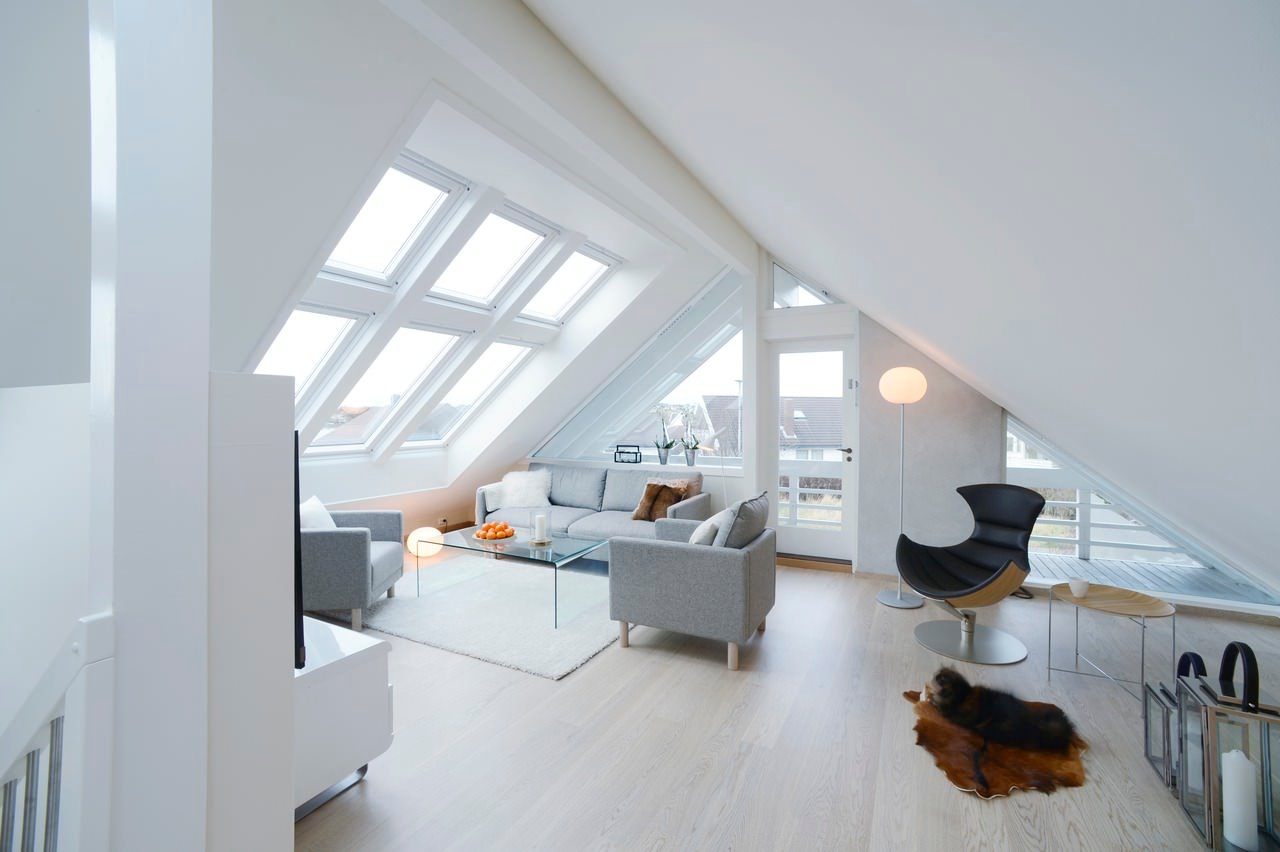 Idee mansarda moderna ben illuminata con luce naturale proveniente dalle grandi finestre. Pareti e soffitti bianchi ed il parquet chiaro per aumentare la luminosità nell'attico. Moderno e elegante.
