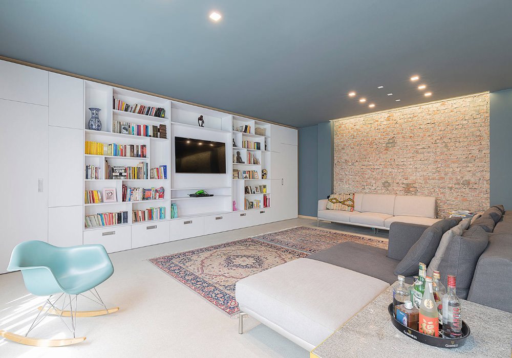 Guida prezzo ristrutturazione casa: soggiorno moderno molto particolare, con pareti e soffitto blu, grande libreria bianca in contrasto con il muro con i mattoni in vista, pavimento bianco