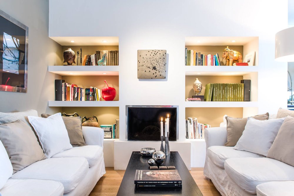 Zona living con parete libreria in cartongesso con camino e nicchie colorate e illuminate. Usato per dividere il soggiorno dalla cucina.