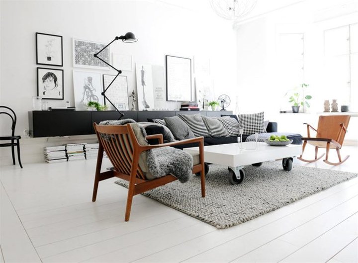 Un salotto scandinavo molto luminoso, in tonalità di bianco, grigio e nero. Pavimento in legno, verniciato in bianco, che aumenta lo spazio visivo